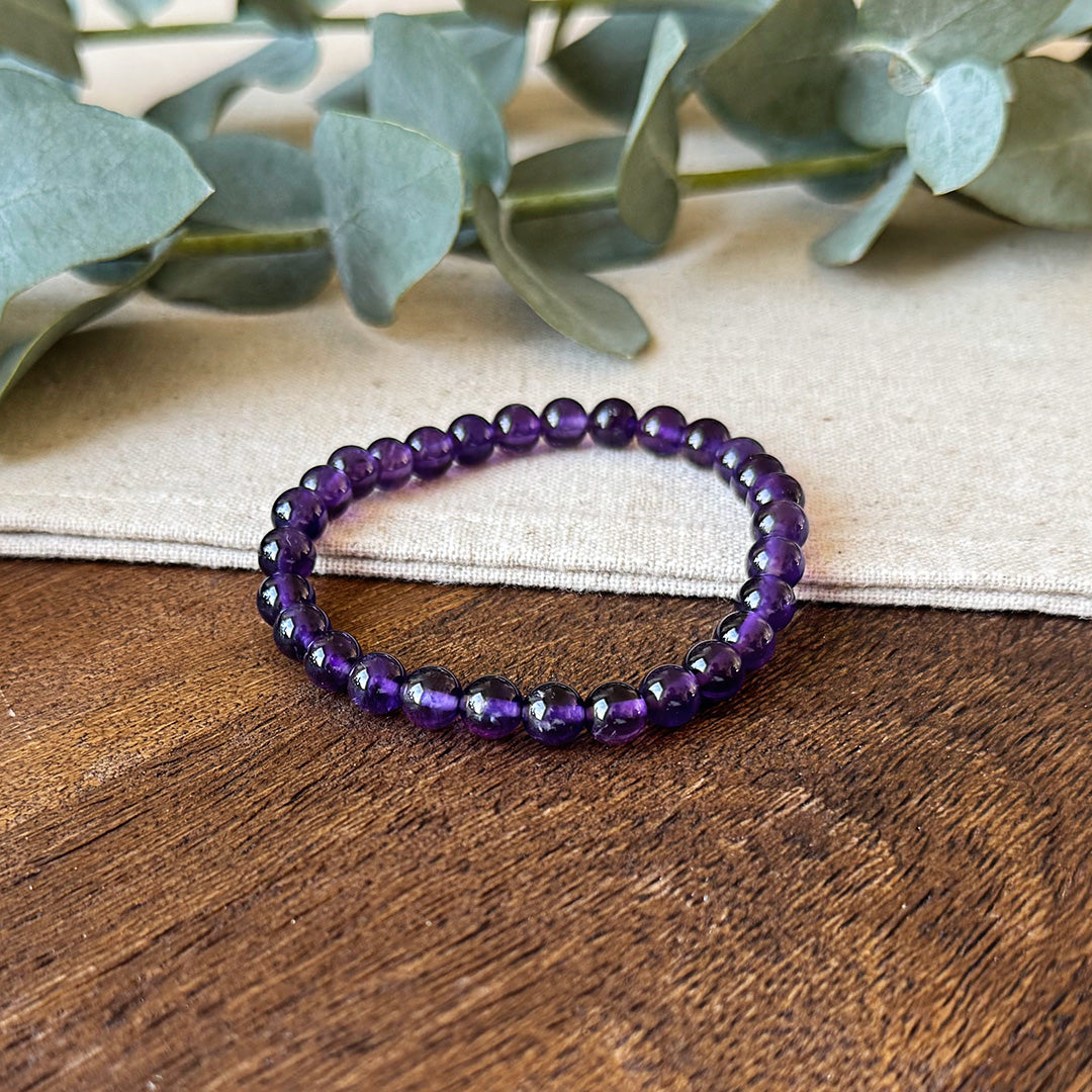 Deep purple Aventari Amethyst Bracelet for clarity and wisdom laid flat on a natural wood and linen surface with eucalyptus leaves.
