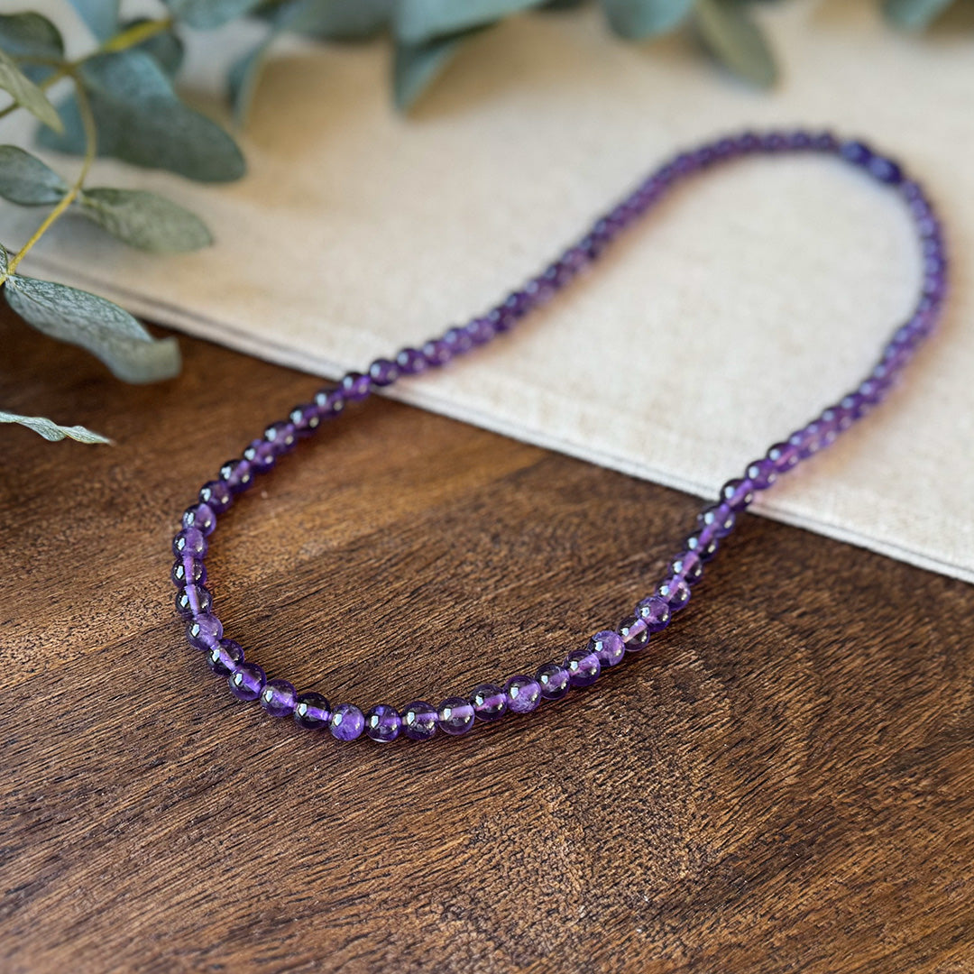 Closer view of the Aventari Amethyst Clarity Necklace showing the vibrant purple beads on a natural wood and linen surface.