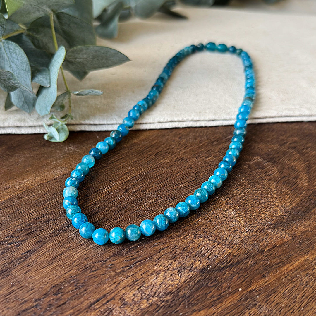 Closer view of the Aventari Apatite Clarity Necklace showing the varied blue-green beads on a wood and linen background.