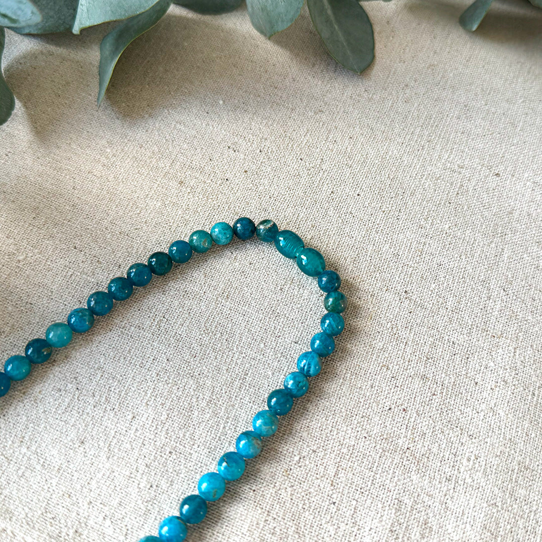Detailed close-up of the screw clasp and blue-green beads of the Aventari Apatite Necklace on a textured linen background.