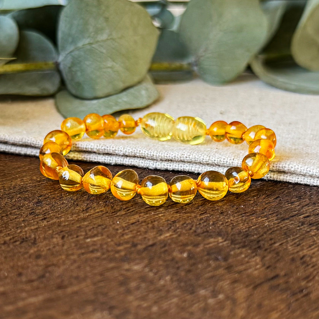 Close-up view of the Aventari Baltic Amber Soothing Bracelet highlighting the smooth, golden beads on a wood and linen surface.