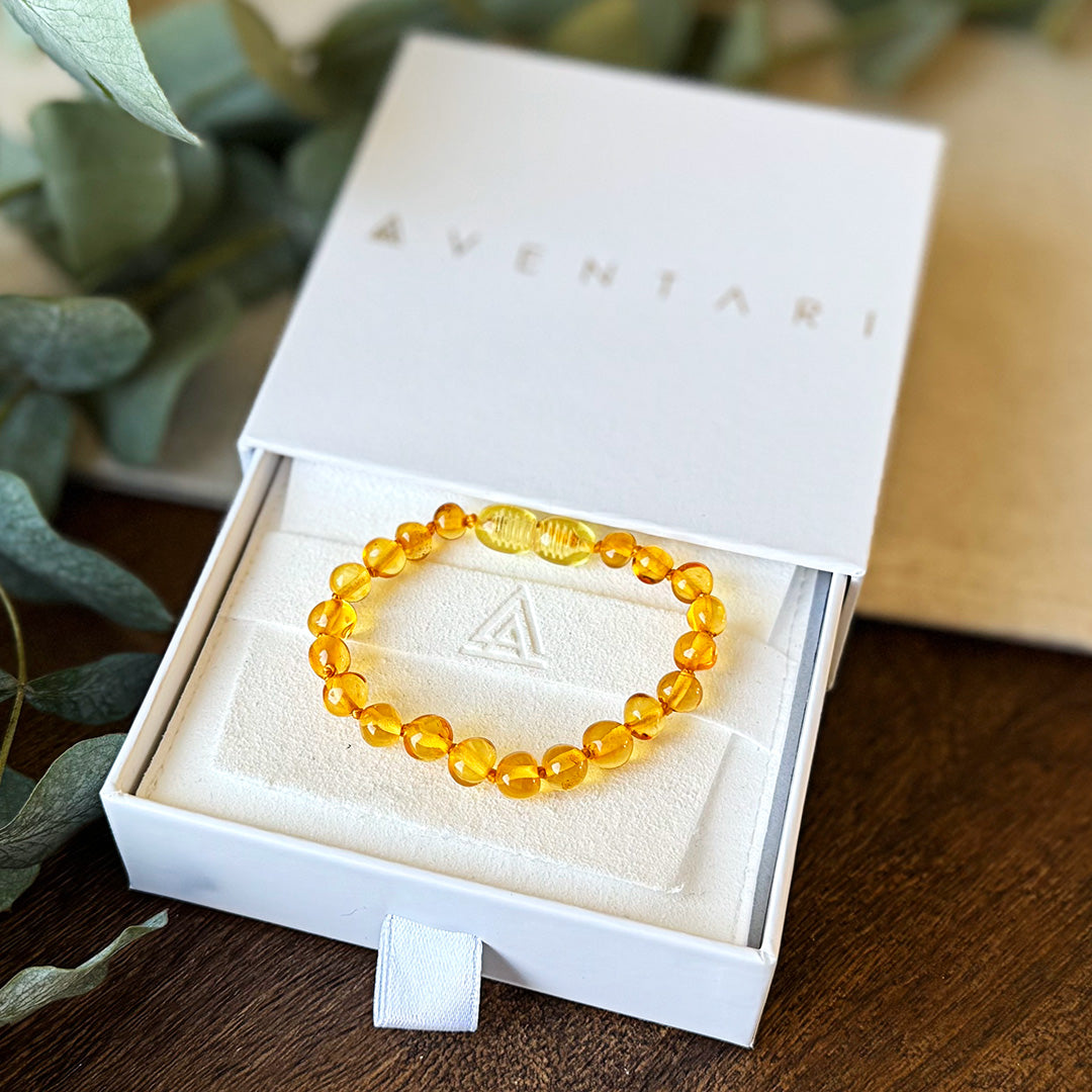 The golden Baltic Amber Soothing Bracelet displayed inside its open white Aventari branded gift box.