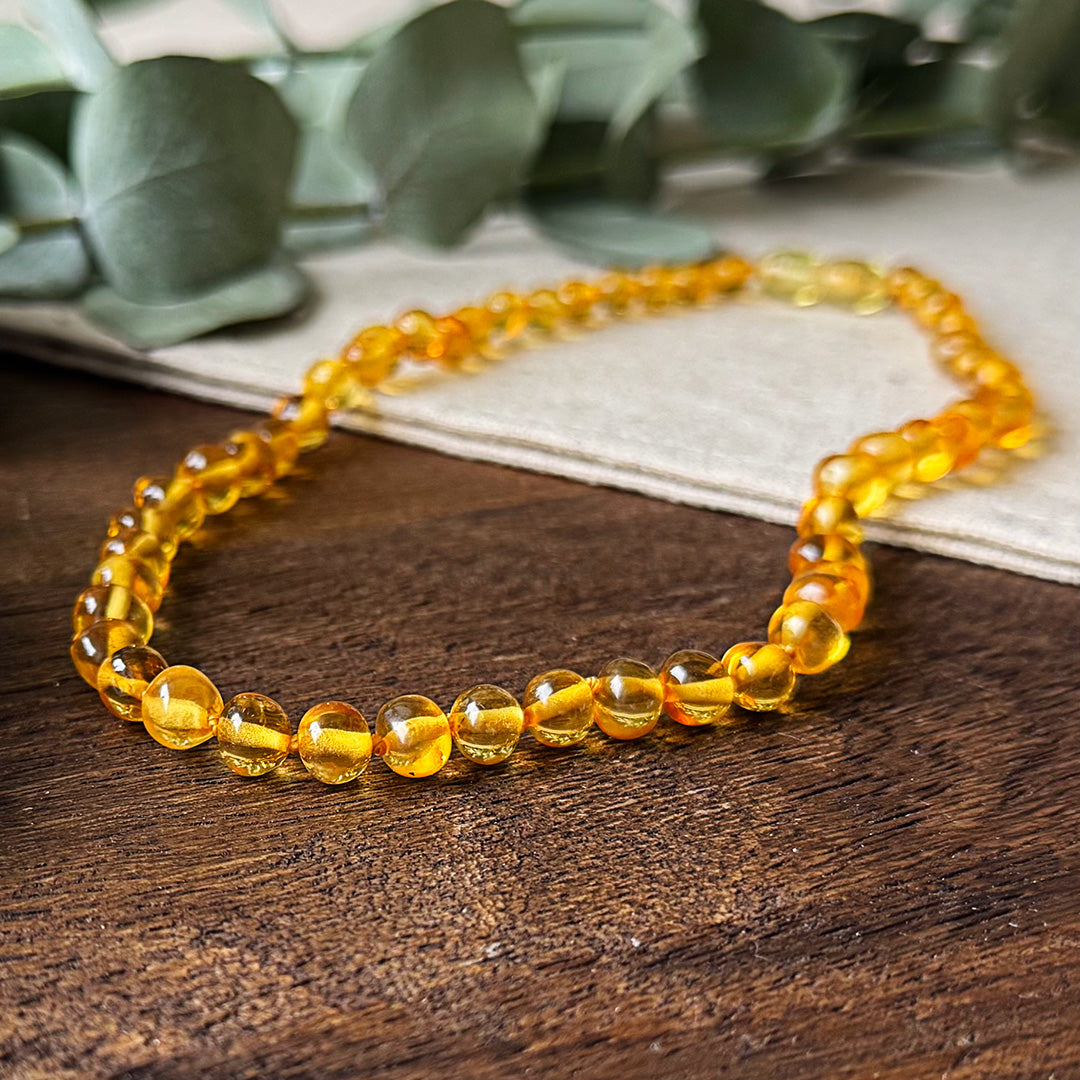 Close-up detail of the smooth, golden-yellow Baltic amber beads of the Aventari Soothing Necklace resting on a textured wood surface.
