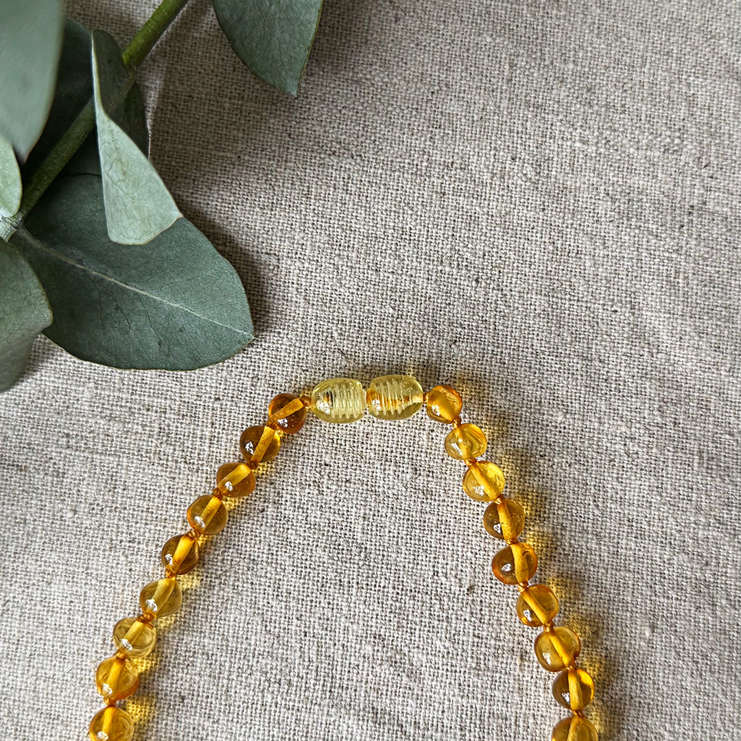 Detailed close-up of the amber-colored screw clasp connecting the Baltic Amber Soothing Necklace, shown on a light linen background.
