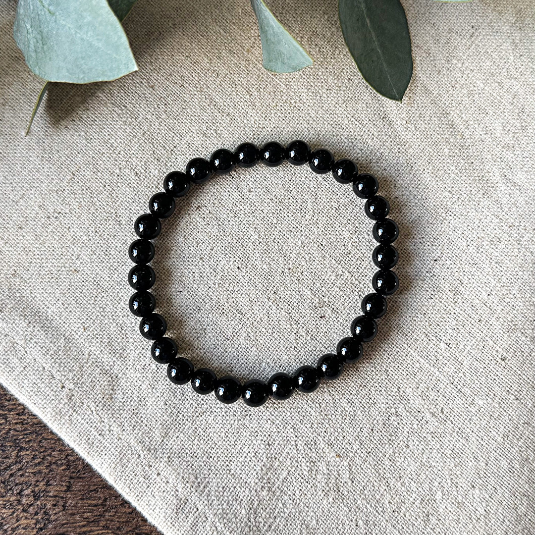 Aventari Black Onyx Focus Bracelet with smooth, black beads arranged in a circle flat lay on a textured linen background.