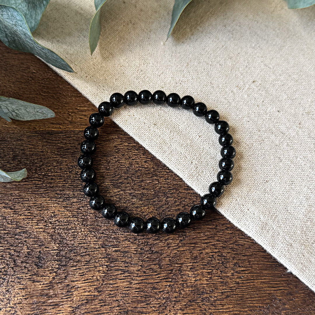 Aventari Black Onyx Focus Bracelet featuring polished black beads laid on a natural wood and linen surface with eucalyptus.