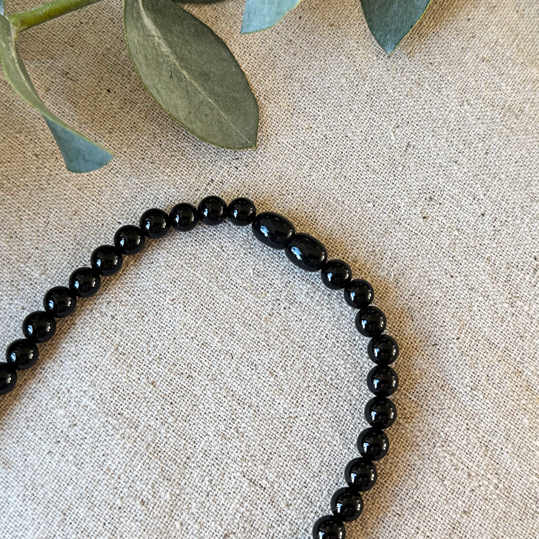 Close-up detail of the barrel clasp and polished black beads of the Aventari Black Onyx Focus Necklace on linen.