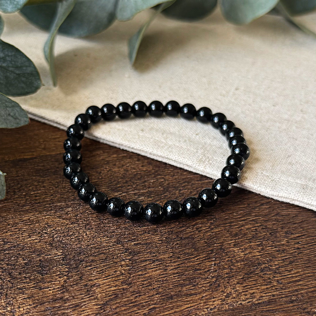 Close-up angle of the Aventari Black Onyx Strength Bracelet showing the polished black beads on a dark wood surface.
