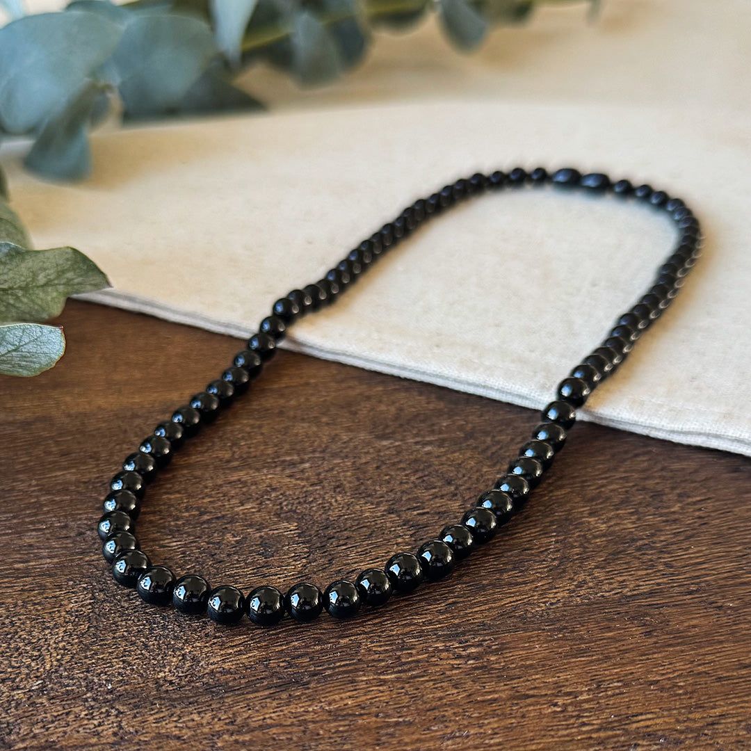 Closer view of the Aventari Black Onyx Strength Necklace showing the smooth, polished black beads on wood and linen.