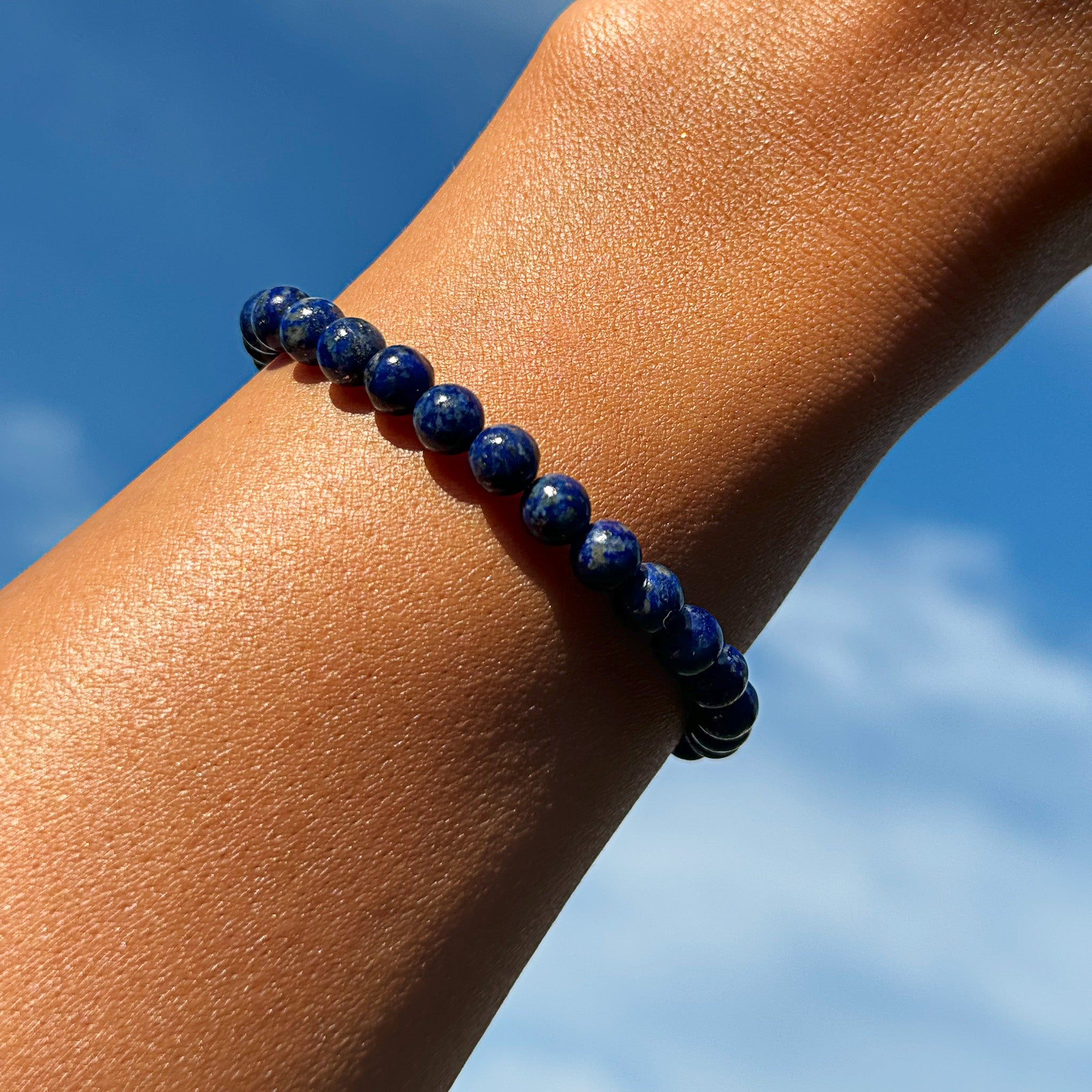 Aventari Lapis Lazuli Protection Bracelet worn on a wrist against a bright blue sky, showcasing its deep blue color.