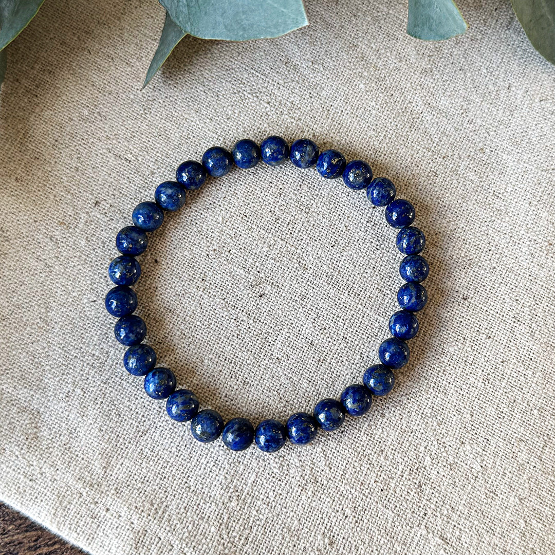 Deep blue Lapis Lazuli Protection Bracelet with gold flecks by Aventari, laid flat in a circle on a textured linen background.