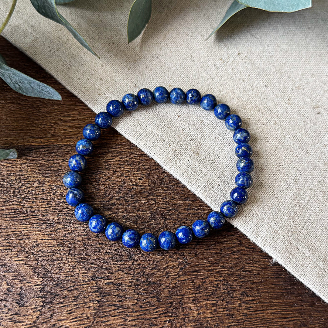 Aventari Lapis Lazuli Protection Bracelet featuring deep blue beads with subtle gold flecks, resting on wood and linen.