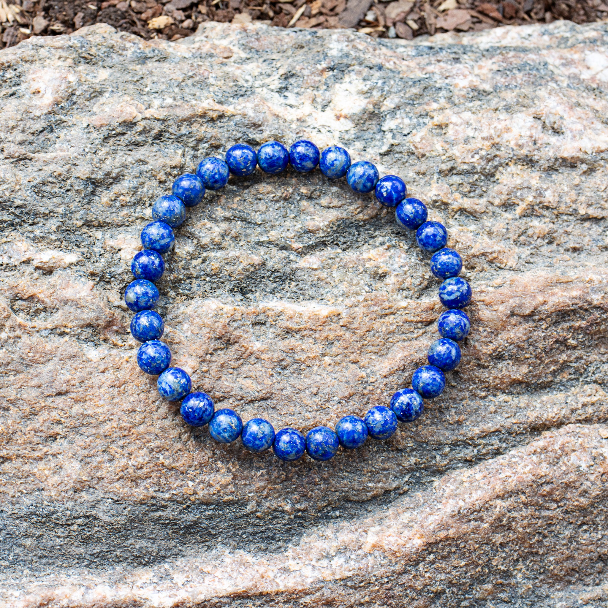 Aventari Lapis Lazuli Psychic Shield Bracelet with deep blue beads resting on a natural, textured rock surface outdoors.