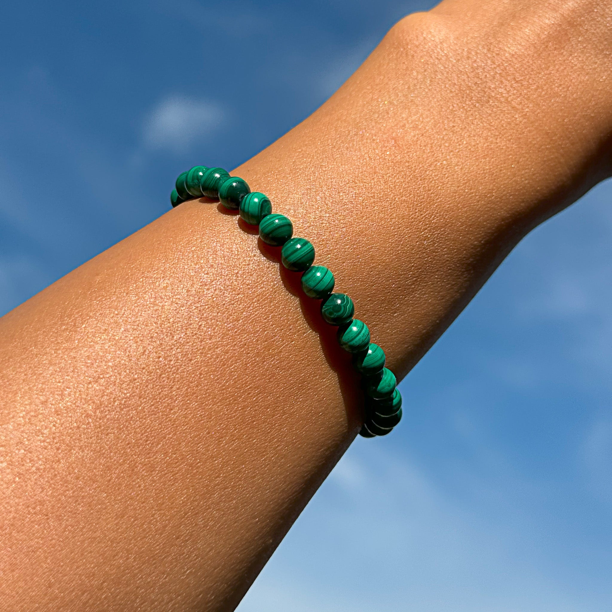 Aventari Malachite Transformation Bracelet worn on a wrist against a bright blue sky, highlighting its vibrant green banded patterns.