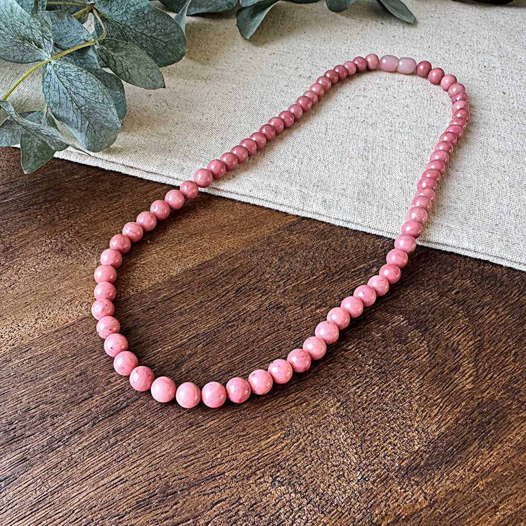 Closer view of the Aventari Rhodonite Self-Love Necklace showing the pink and grey tones in the beads on wood and linen.