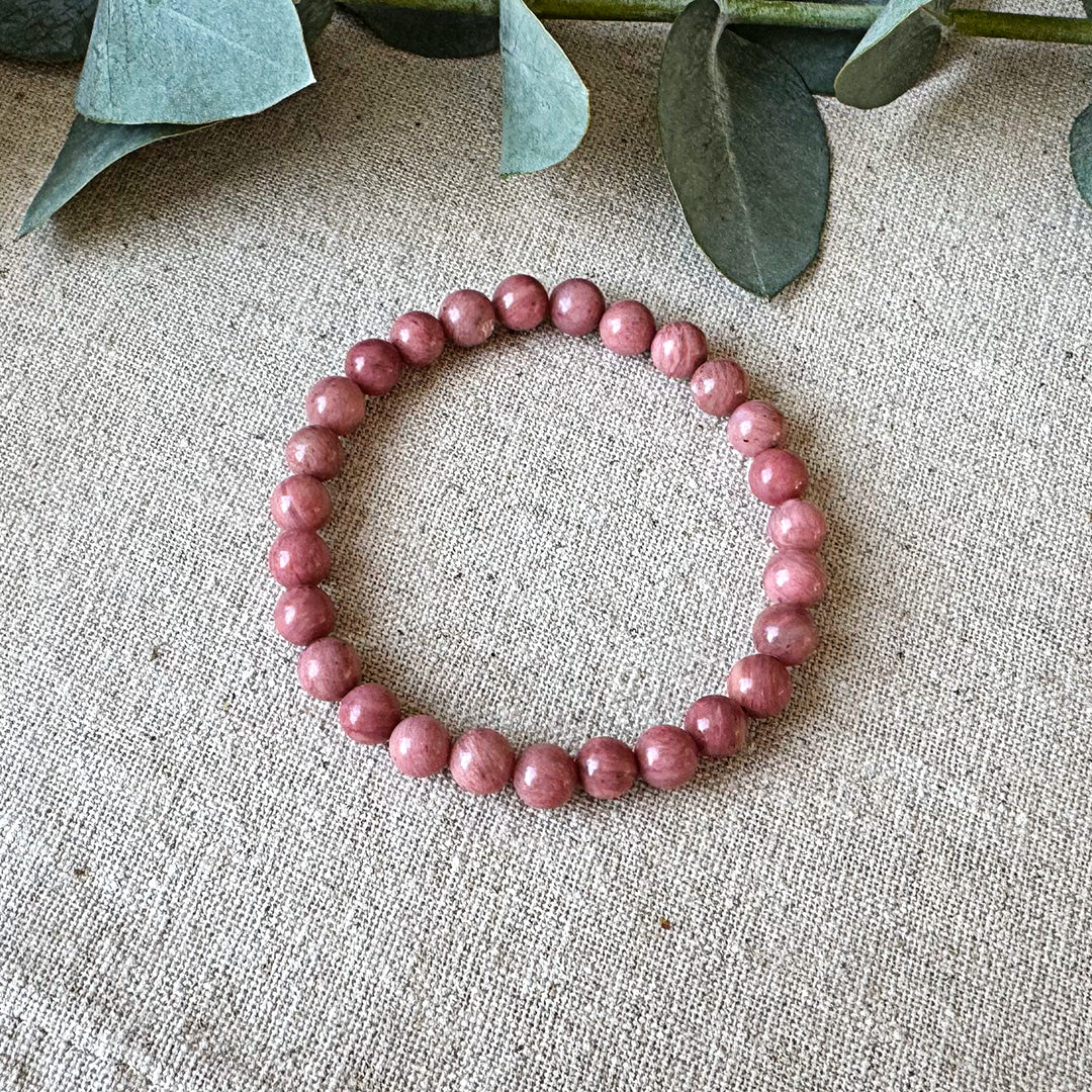Pink and grey Rhodonite Wellness Bracelet by Aventari laid flat in a circle on a textured linen background.
