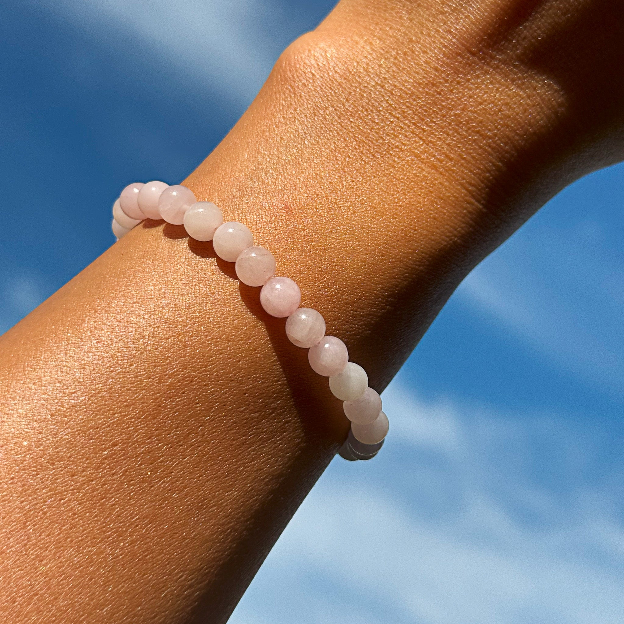 Aventari Rose Quartz Bracelet for universal love worn on a wrist against a bright blue sky, highlighting its gentle pink color.