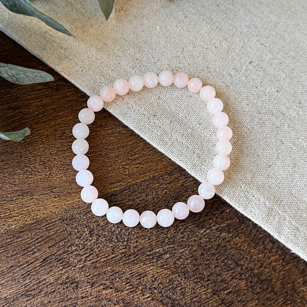 Aventari Rose Quartz Love Bracelet featuring soft pink beads resting on a natural wood and linen surface with eucalyptus.