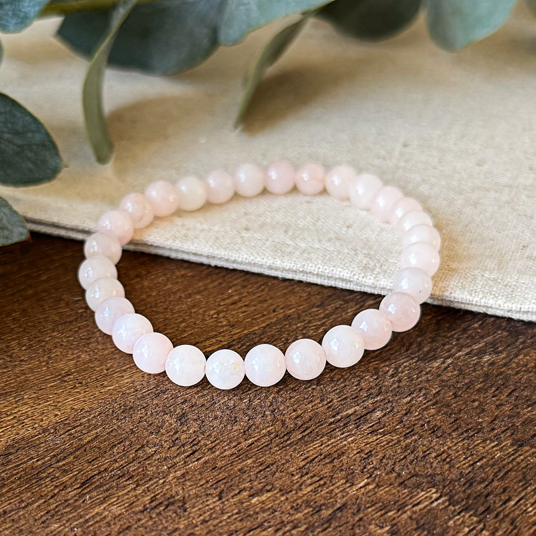 Close-up view of the Aventari Rose Quartz Self-Love Bracelet showing the gentle pink beads on a dark wood surface.