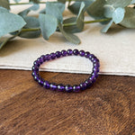 Deep purple Aventari Amethyst Bracelet for clarity and wisdom laid flat on a natural wood and linen surface with eucalyptus leaves.