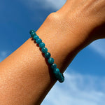 Aventari Apatite Bracelet with varying blue-green beads worn on a wrist, shown against a clear blue sky to symbolize mental clarity.