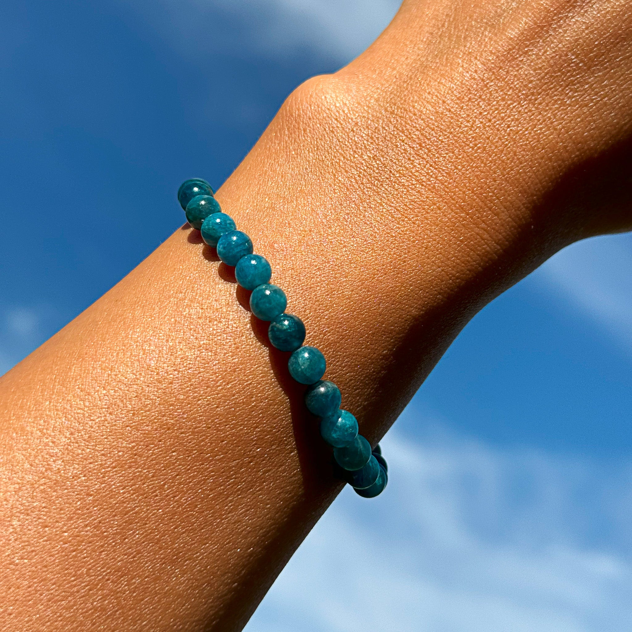Aventari Apatite Bracelet with varying blue-green beads worn on a wrist, shown against a clear blue sky to symbolize mental clarity.