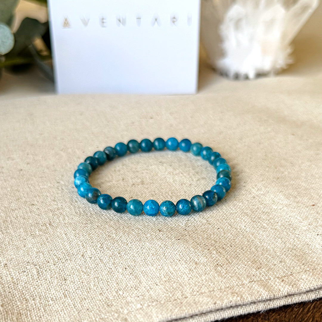 Close-up detail of the Aventari Apatite Clarity Bracelet's blue-green beads on a linen background, with the gift box softly blurred behind.