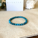 Close-up detail of the Aventari Apatite Clarity Bracelet's blue-green beads on a linen background, with the gift box softly blurred behind.