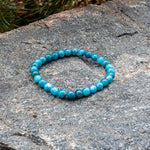 The blue-green Aventari Apatite Focus Bracelet displayed naturally on a textured granite rock outdoors.