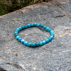 The blue-green Aventari Apatite Focus Bracelet displayed naturally on a textured granite rock outdoors.