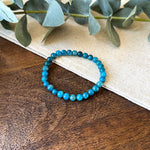 Aventari Apatite Intellect Bracelet featuring blue-green beads laid flat on a natural wood and linen surface with eucalyptus accents.
