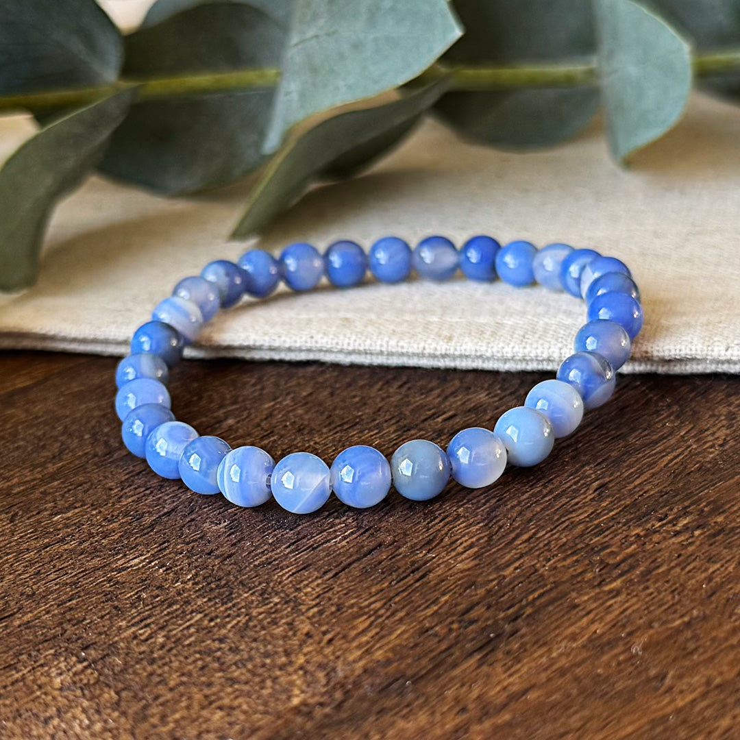 Close-up detail of the pale blue banded beads of the Aventari Blue Lace Agate Communication Bracelet on a wood surface.