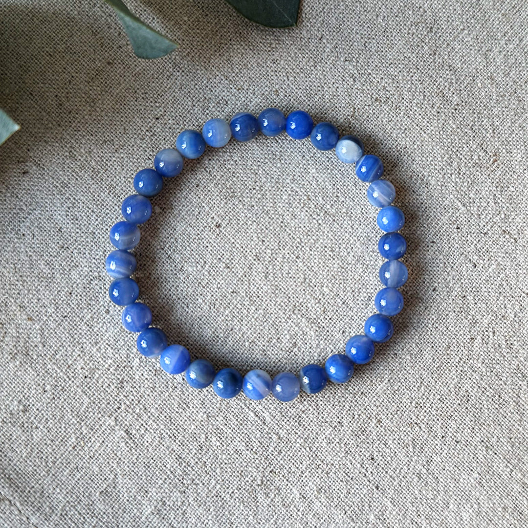 Pale blue banded Blue Lace Agate Communication Bracelet by Aventari laid flat in a circle on a textured linen background.