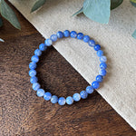 Aventari Blue Lace Agate Communication Bracelet with banded pale blue beads resting on a natural wood and linen background.