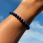 Aventari Lapis Lazuli Protection Bracelet worn on a wrist against a bright blue sky, showcasing its deep blue color.