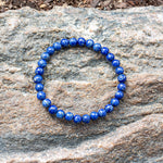 Aventari Lapis Lazuli Psychic Shield Bracelet with deep blue beads resting on a natural, textured rock surface outdoors.